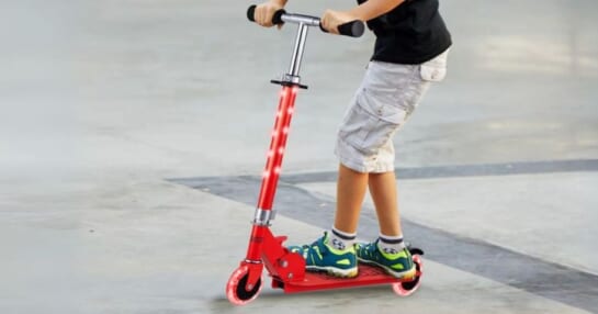 a little boy riding a red light up kick scooter
