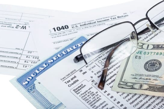 A pair of glasses, a twenty-dollar bill, and a Social Security card, set atop federal income tax forms.